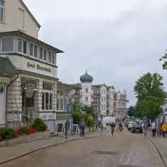 Ulica w Ahlbecku z hotelami i kawiarniami. Widać hotel Meerwelle, kawiarnię z lodami i ludzi spacerujących po chodniku.