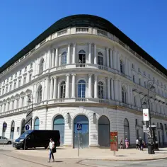 Elegancki budynek, być może najdroższy hotel w Polsce, z białymi kolumnami i łukowymi oknami, na tle błękitnego nieba.