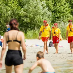 Ratownicy czuwają nad bezpieczeństwem na wakacjach. Na plaży widać ludzi odpoczywających i bawiących się.