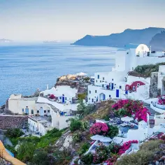 Widok na białe domy Santorini z niebieskimi drzwiami i oknami, kwitnące bugenwille. Czy do Grecji potrzebny jest paszport? Tak, jeśli nie jesteś obywatelem UE.