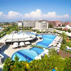 Luksusowy hotel z basenami w Kizilagac, z palmami i zielenią, pod błękitnym niebem z chmurami.