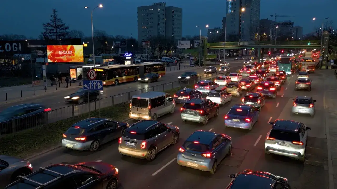 Warszawa dzisiaj: wieczorny korek na ulicy, światła samochodów i autobusu tworzą świetlny szlak.