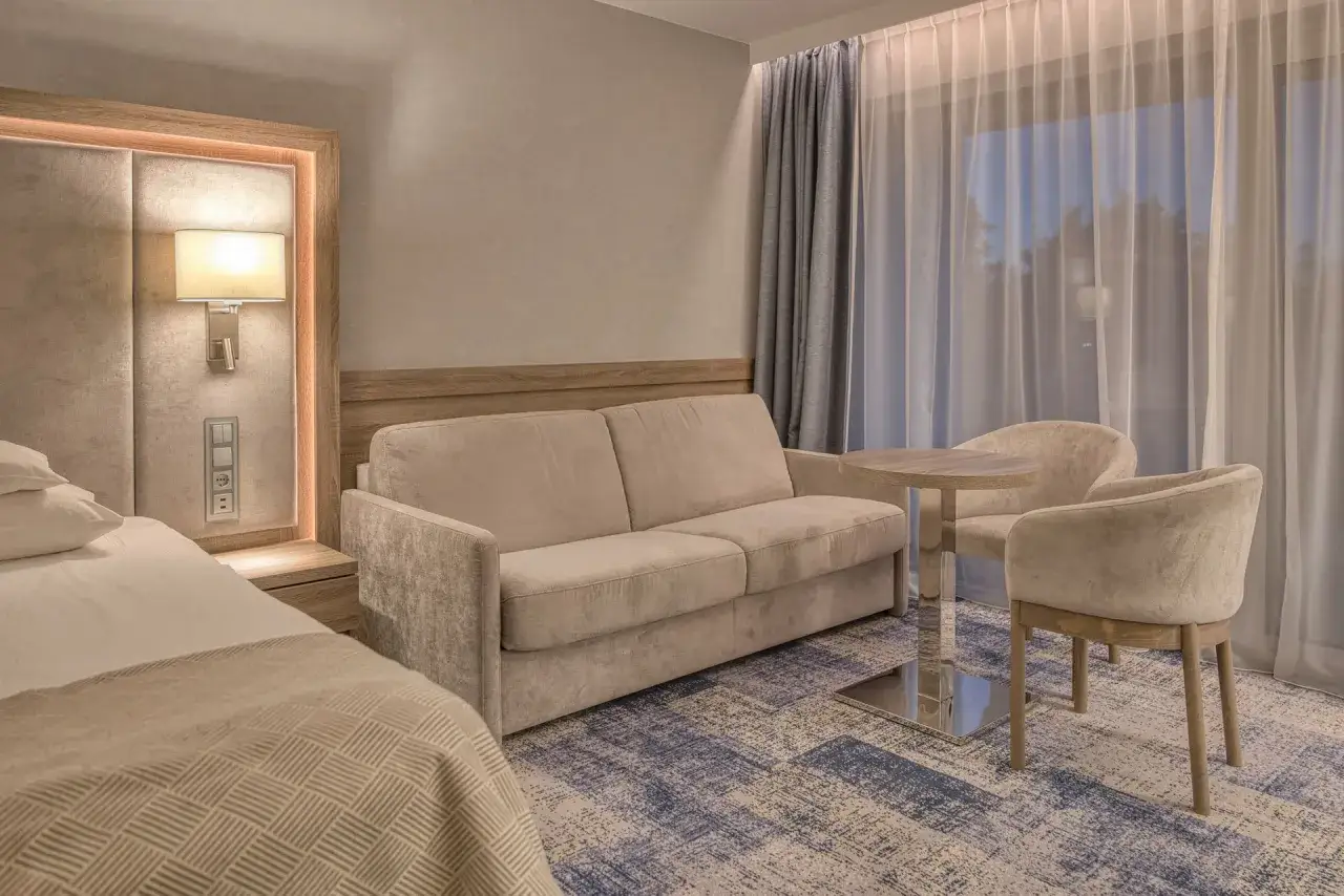 Elegancki pokój w hotelu 5 gwiazdkowym: wygodna sofa, stolik z krzesłami i łóżko.