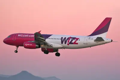 Samolot Wizz Air z różowym dziobem i fioletowym ogonem wznosi się na tle różowego nieba. Wizz priority to szybka droga do celu.